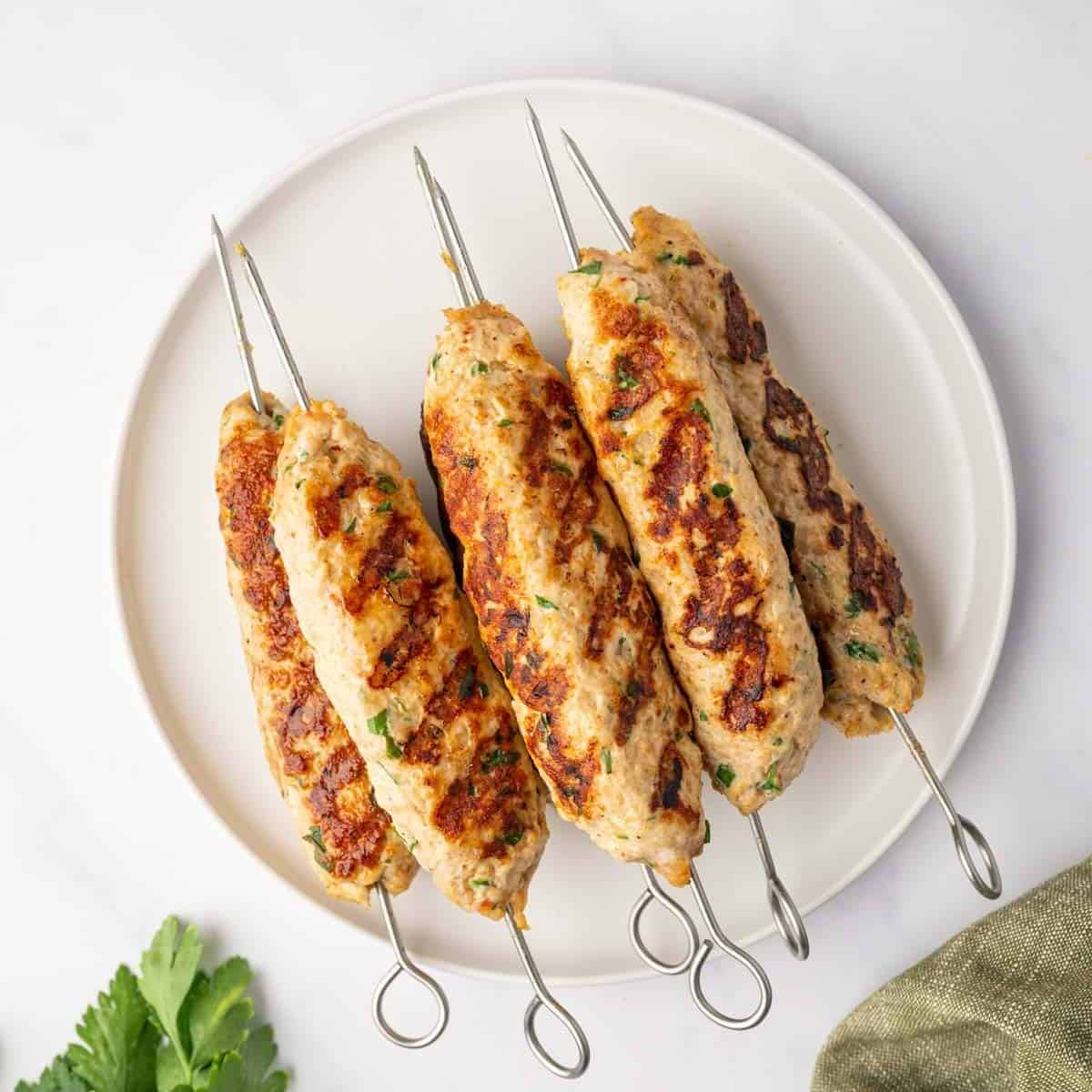 Grilled chicken kofta skewers are on a platter.