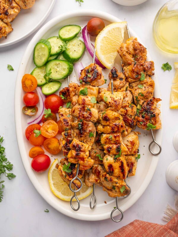 Fresh veggies and lemon wedges surround grilled chicken skewers on a platter.