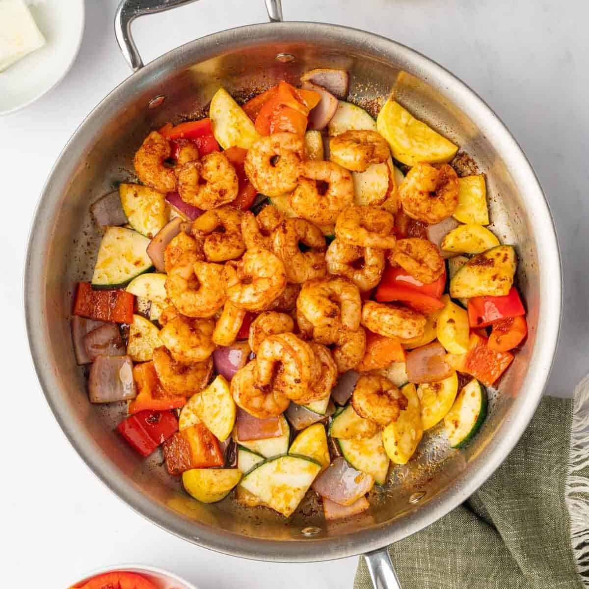 Sauteed shrimp added ove sauteed vegetables in a skillet.