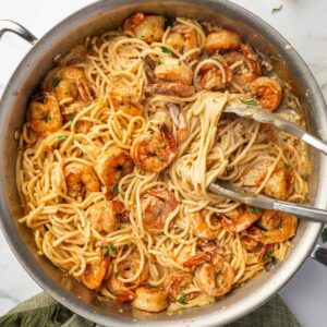 Tongs scoop up a serving of cajun shrimp pasta.