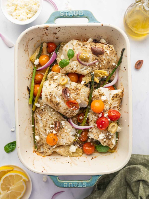 Seasoned cod fish in a rectangle baking dish with asparagus, tomatoes and onions.